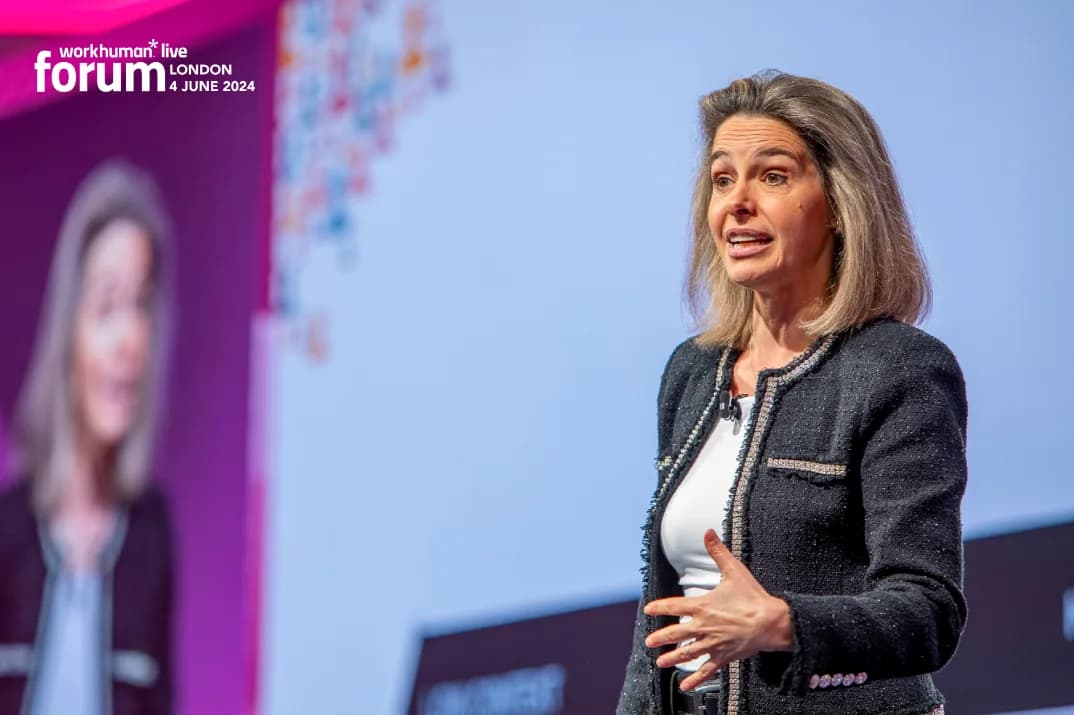 A woman with shoulder-length hair is speaking at the Workhuman Live Forum in London on June 4, 2024. She appears engaged and animated, gesturing with her hands as she addresses the audience. The background features a colorful design alongside text that includes the event name and date.