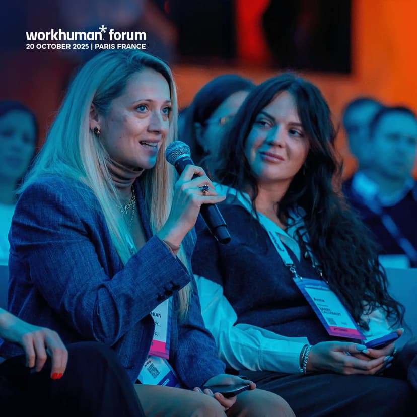 A woman speaking into a microphone at a Workhuman forum event. She has long hair and is wearing a blazer. A seated audience can be seen in the background, with another woman beside her holding a smartphone. The event details are visible at the top, indicating it took place on October 20, 2025, in Paris, France.